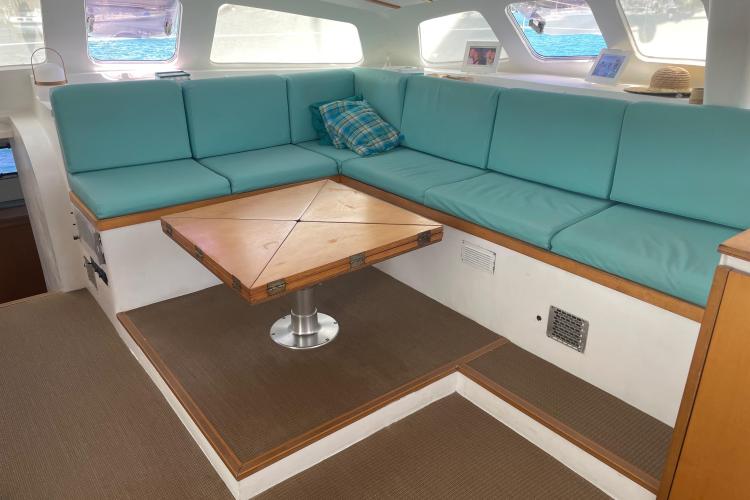 Cozy boat interior with teal cushions, wooden table, and large windows. Custom KSENIA 149, 2010 model.