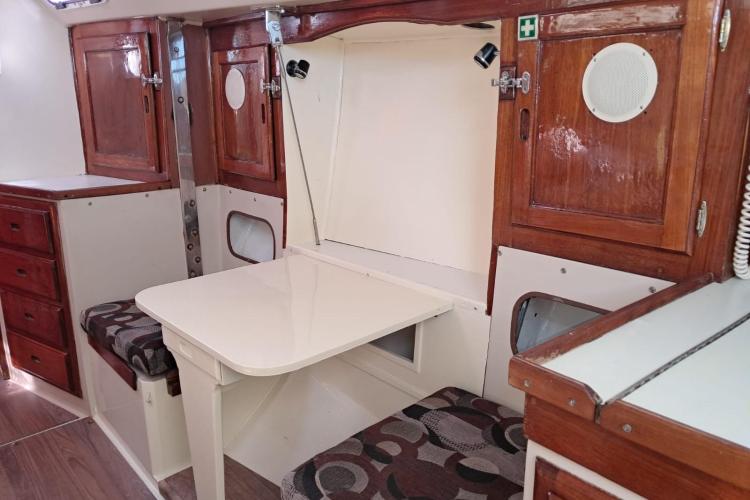 1986 Dufour CATALINA yacht interior with foldable table, wooden cabinets, and cushioned seating.