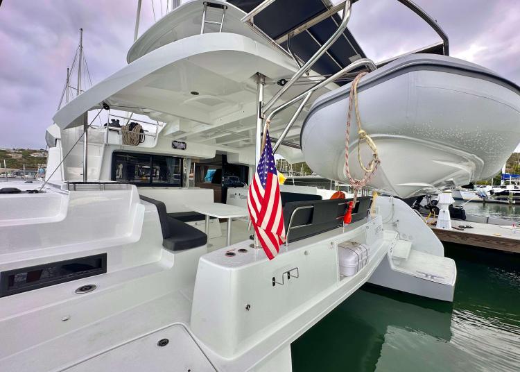 2023 Lagoon 46 catamaran with American flag, docked at marina, featuring spacious deck and tender.