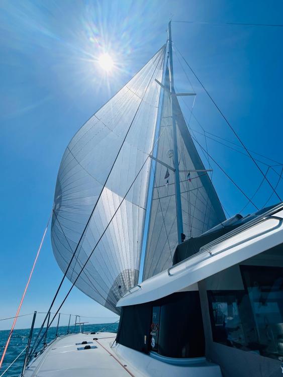 2024 Excess 14 sailboat with full sails under bright sun and clear blue sky.