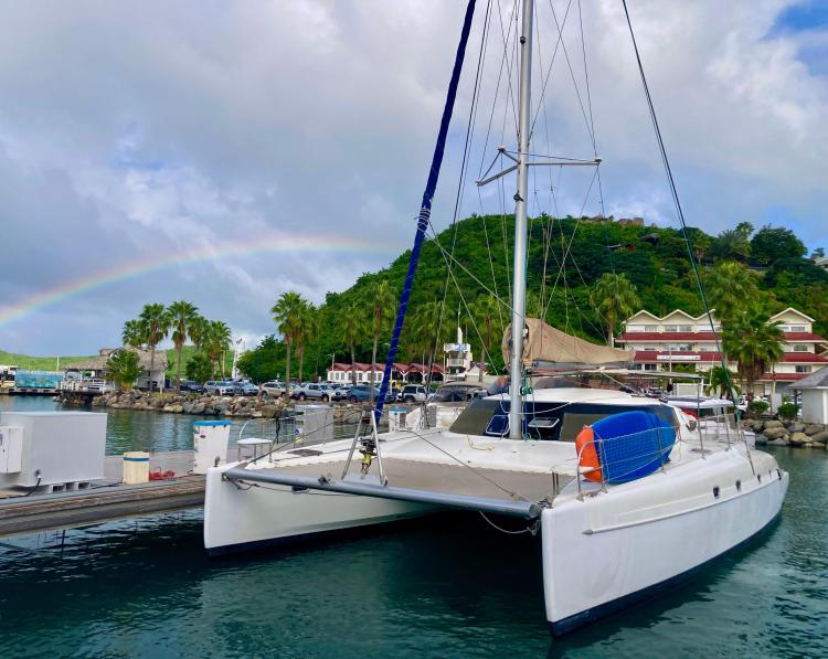 2006 Fountaine Pajot Bahia 46 catamaran docked with rainbow and tropical backdrop.