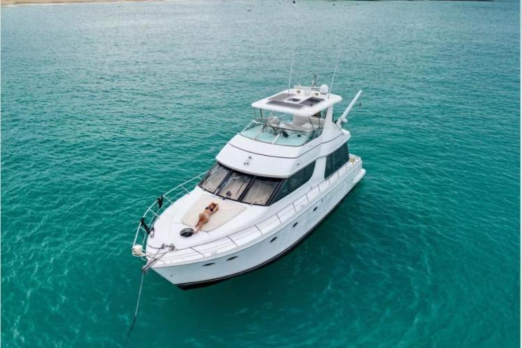 2000 Carver 530 Voyager Pilothouse yacht on turquoise water, person sunbathing on deck.