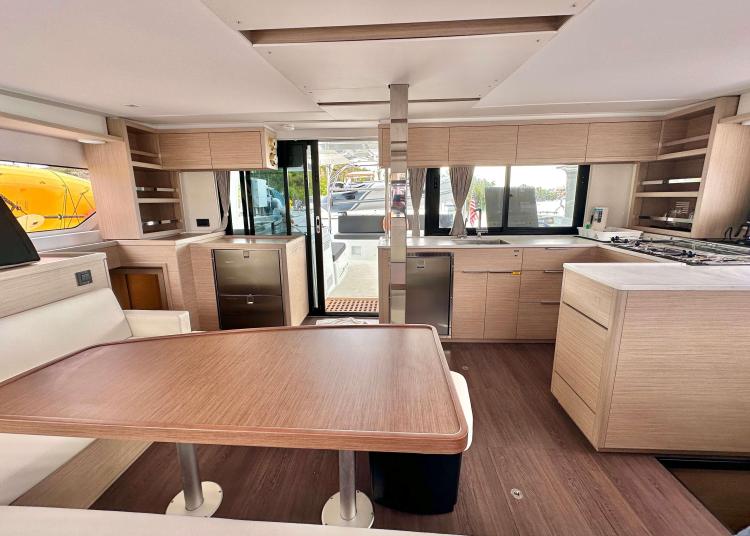 Interior of 2023 Lagoon 46 yacht, featuring modern kitchen and dining area with wood finishes.