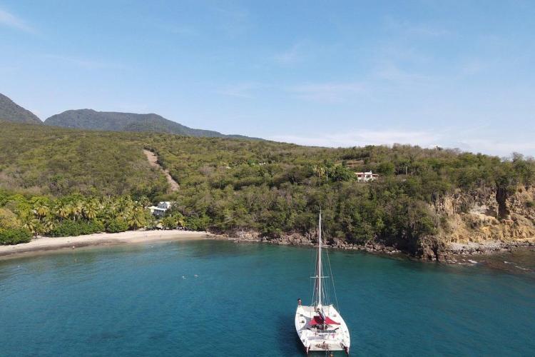 Aerial view of 1995 Catamaran Day Charter near tropical beach and lush hillside.