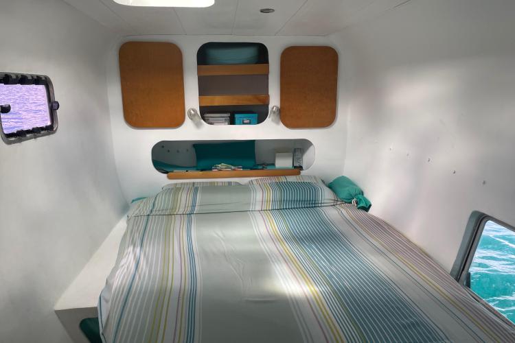 Cozy interior of Custom KSENIA 149 boat, featuring a neatly made bed and wooden accents.