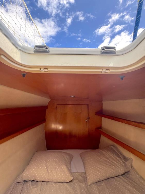 Cabin interior of 2006 Fountaine Pajot Bahia 46 catamaran with cozy bedding and wooden shelves.
