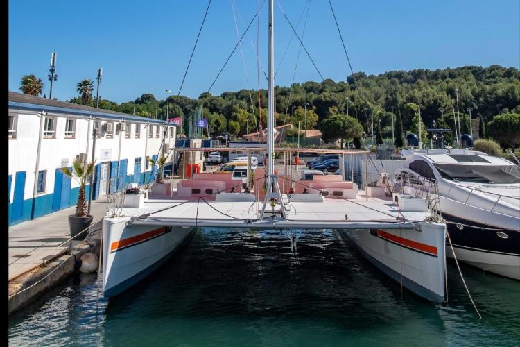 Modern 2026 Custom DAYCHARTER catamaran docked at marina, surrounded by yachts and lush greenery.