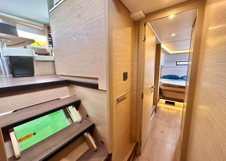 2023 Lagoon 46 yacht interior with modern wood finish, hallway, and cozy bedroom.